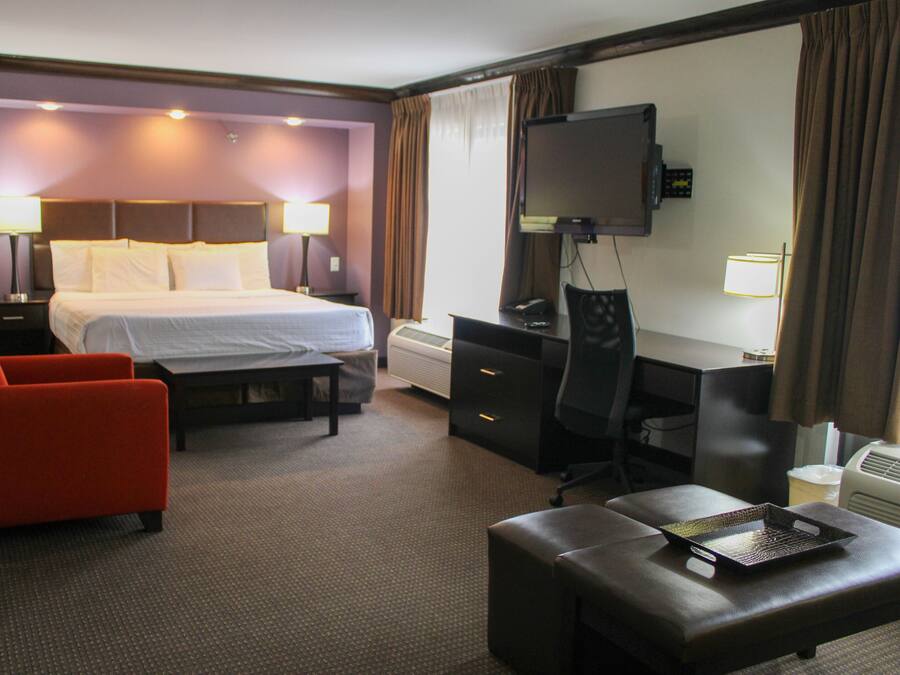 Ett hotellrum med en säng, ett skrivbord, en stol, en tv och ett litet bord.