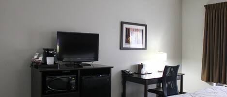 A hotel room with a bed, a desk with a chair, a television, a microwave, and a coffee maker.