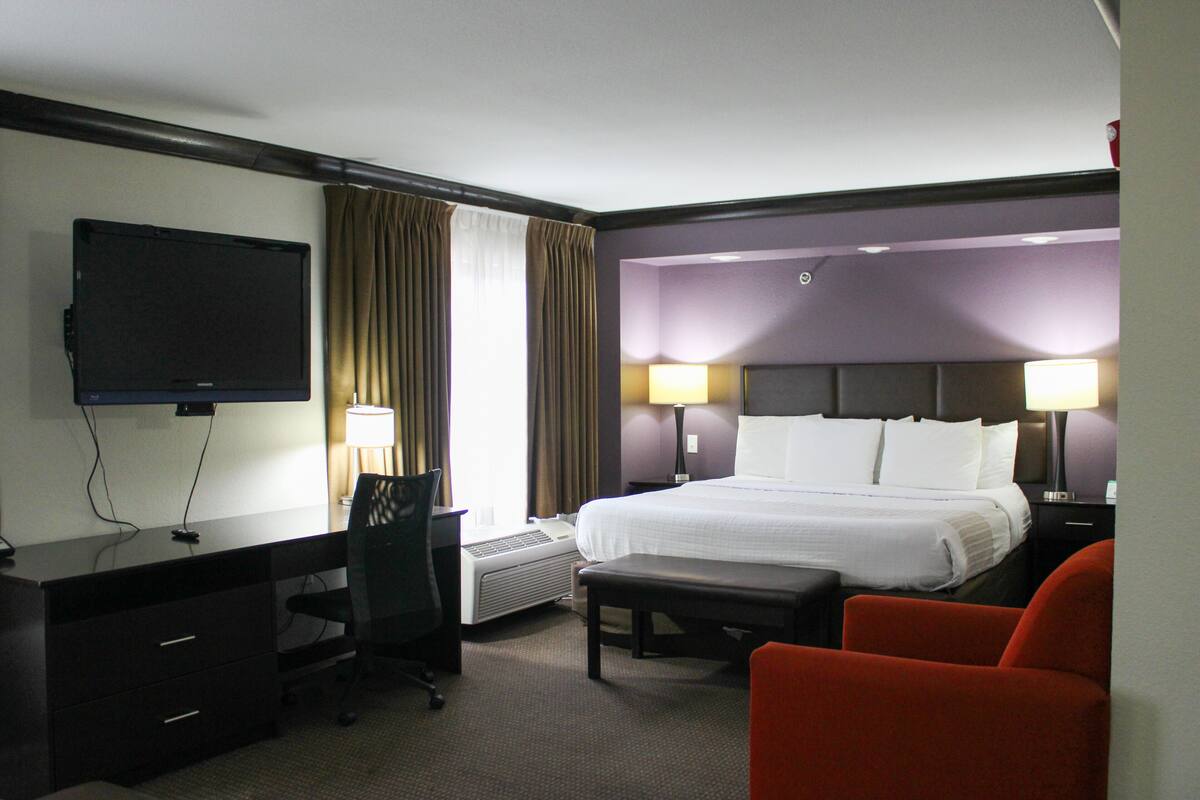 A hotel room with a bed, desk, chair, and a television.