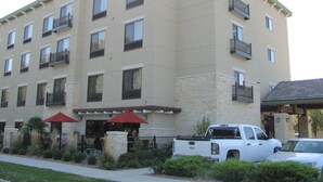 Un hôtel à plusieurs étages doté de balcons, d’une façade en pierre et d’un parking où est garé un pick-up blanc.