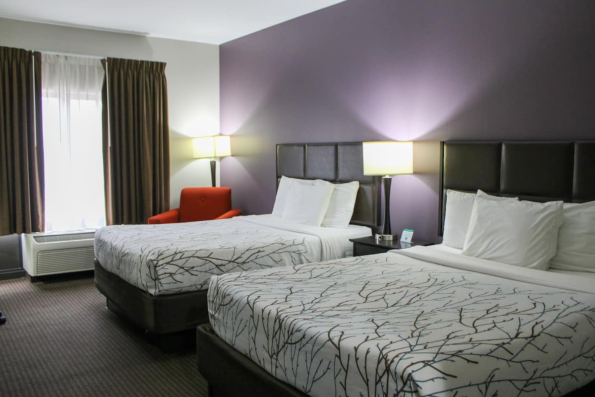 A hotel room with two beds, a chair, and a nightstand with lamps.