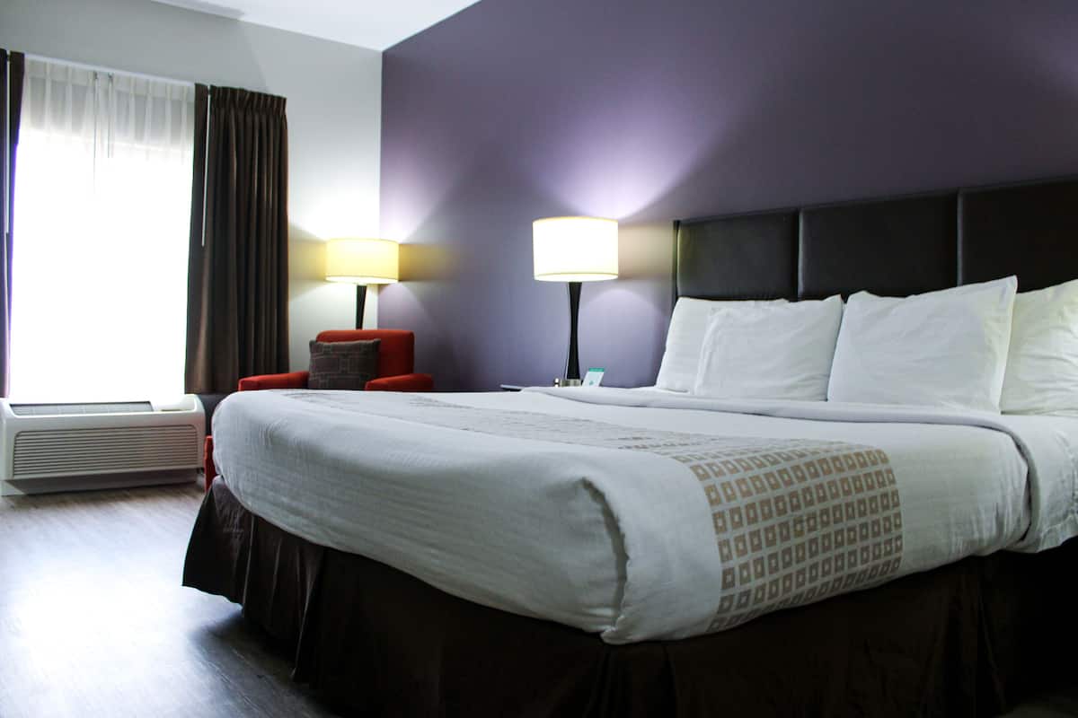 A hotel room with a large bed, two bedside lamps, a red chair, and a window with curtains.