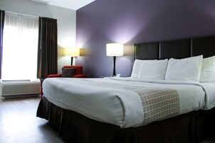 Una habitación de hotel con una cama grande, dos lámparas de noche, una silla roja y una ventana con cortinas.
