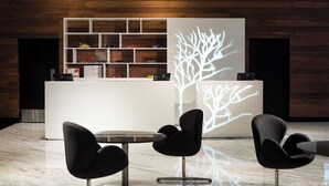 Un espace d’accueil moderne avec un bureau blanc, des chaises noires et une projection d’un arbre sur le mur.