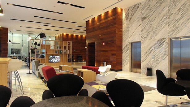 Un hall d’entrée moderne avec un comptoir d’accueil en bois, des sièges confortables, un téléviseur et un mur en marbre.