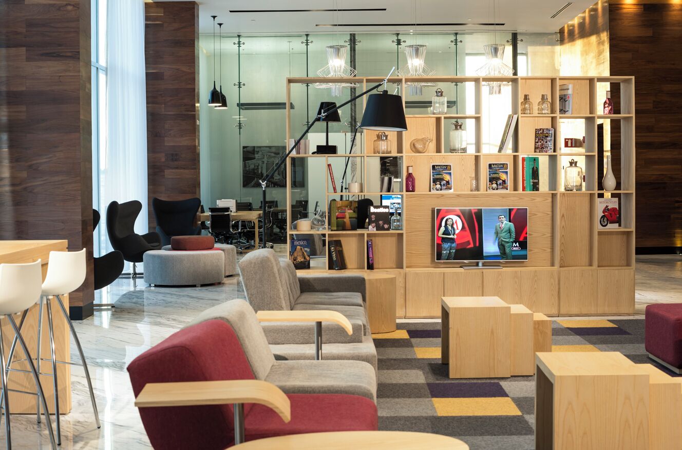 Ett modernt loungeområde med sittplatser, en tv och en bokhylla i trä med diverse föremål.