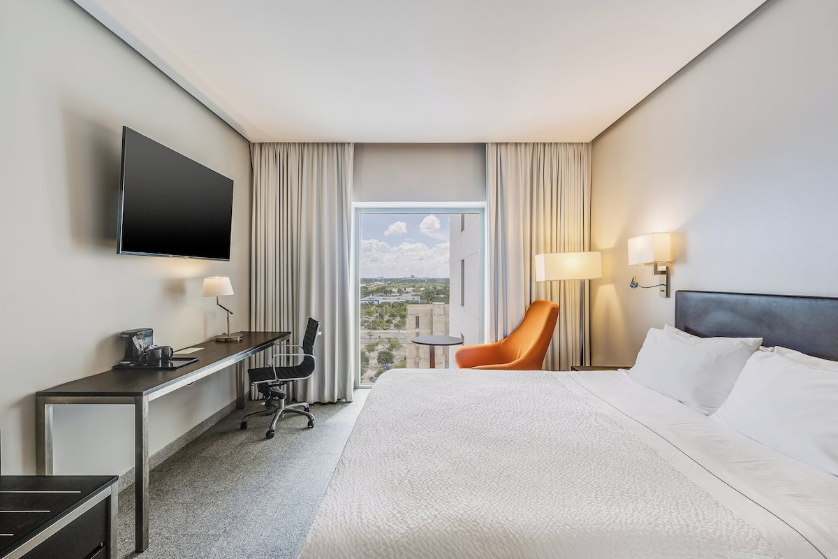 Habitación de hotel con cama, escritorio, silla, televisión y vista a la ciudad.