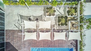 Vue aérienne d’un espace piscine aménagé sur un toit, avec une piscine, des parasols et des jardinières.