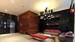 Un hall d’entrée moderne avec un mur d’accent en bois, un banc rouge, des canapés gris avec des coussins rouges et un lustre.