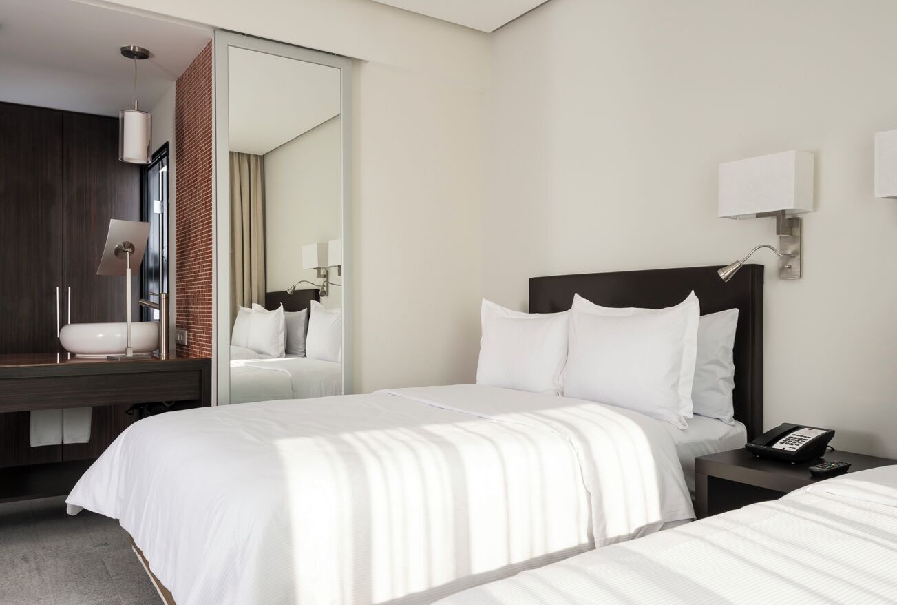 Habitación de hotel con una cama grande, una mesita de noche con un teléfono, un espejo y un baño visible a través de una puerta abierta.