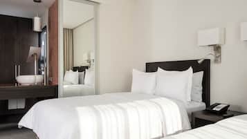 Habitación de hotel con una cama grande, una mesita de noche con un teléfono, un espejo y un baño visible a través de una puerta abierta.