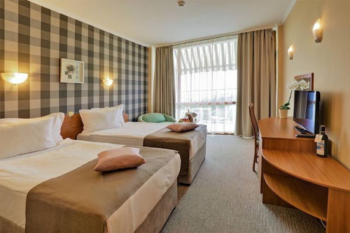 A hotel room with two beds, a desk, a television, and a window with curtains.