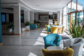 Een ruime lobby met modern zitmeubilair, een bar en grote ramen met uitzicht op buiten.