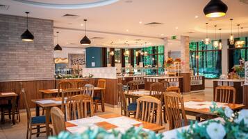Un restaurante con mesas y sillas de madera, iluminación colgante y vistas al bosque a través de amplios ventanales.