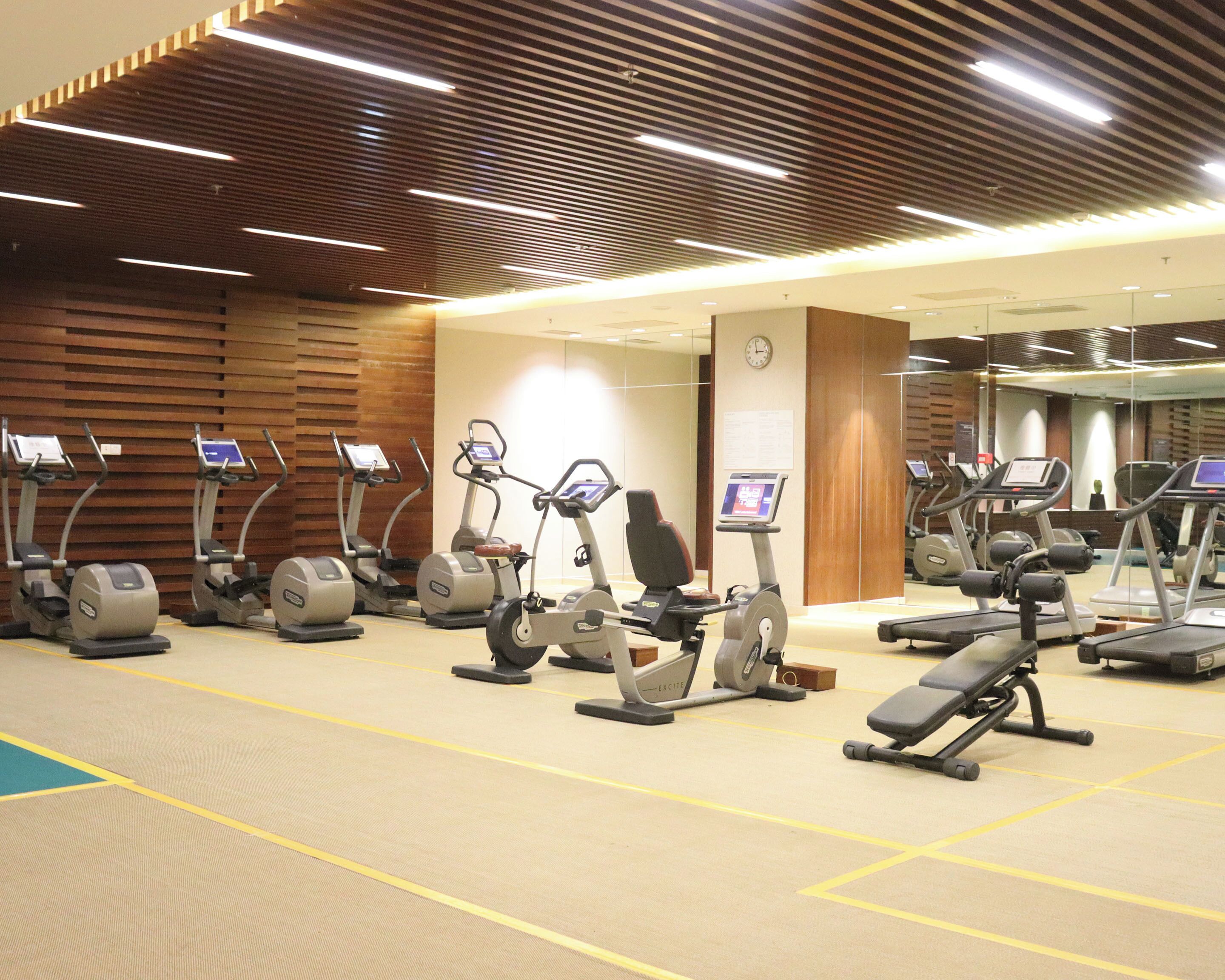 A gym with multiple cardio machines, a mirrored wall, and a clock on the wall.