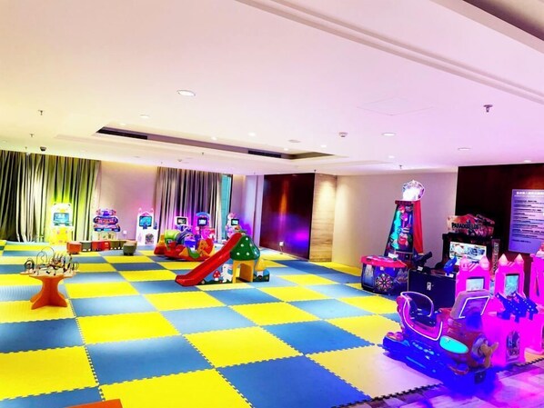 Zona de juegos infantiles con alfombras de colores, un tobogán y varios juegos de arcade.