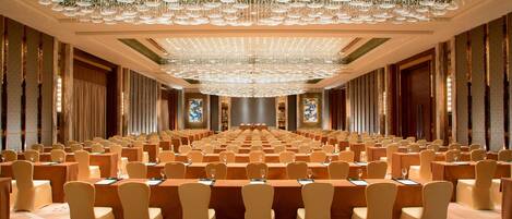 A large conference room with rows of tables and chairs, a grand chandelier, and large windows with curtains.