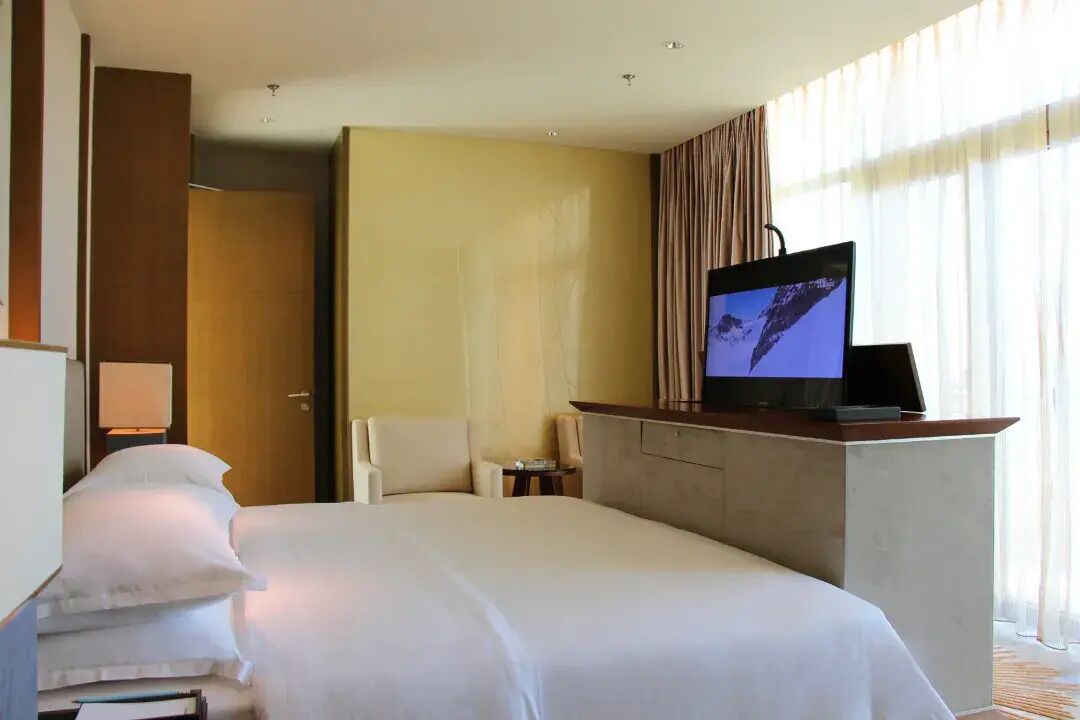 A hotel room with a bed, a television on a stand, a desk, and a chair.