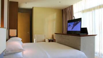 A hotel room with a bed, a television on a stand, a desk, and a chair.