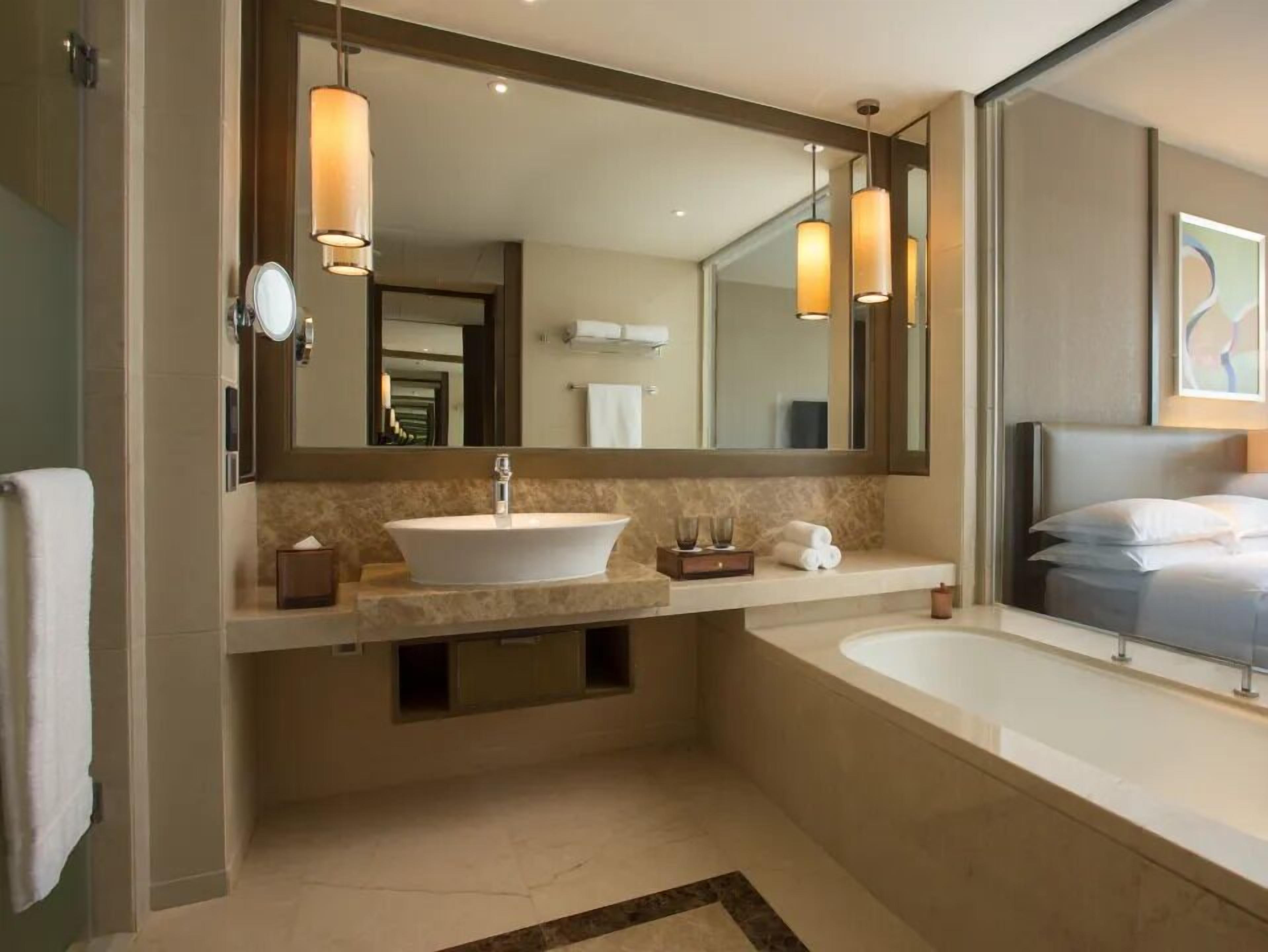 A modern bathroom with a large oval sink, a bathtub, and a large mirror. There are two pendant lights above the mirror.