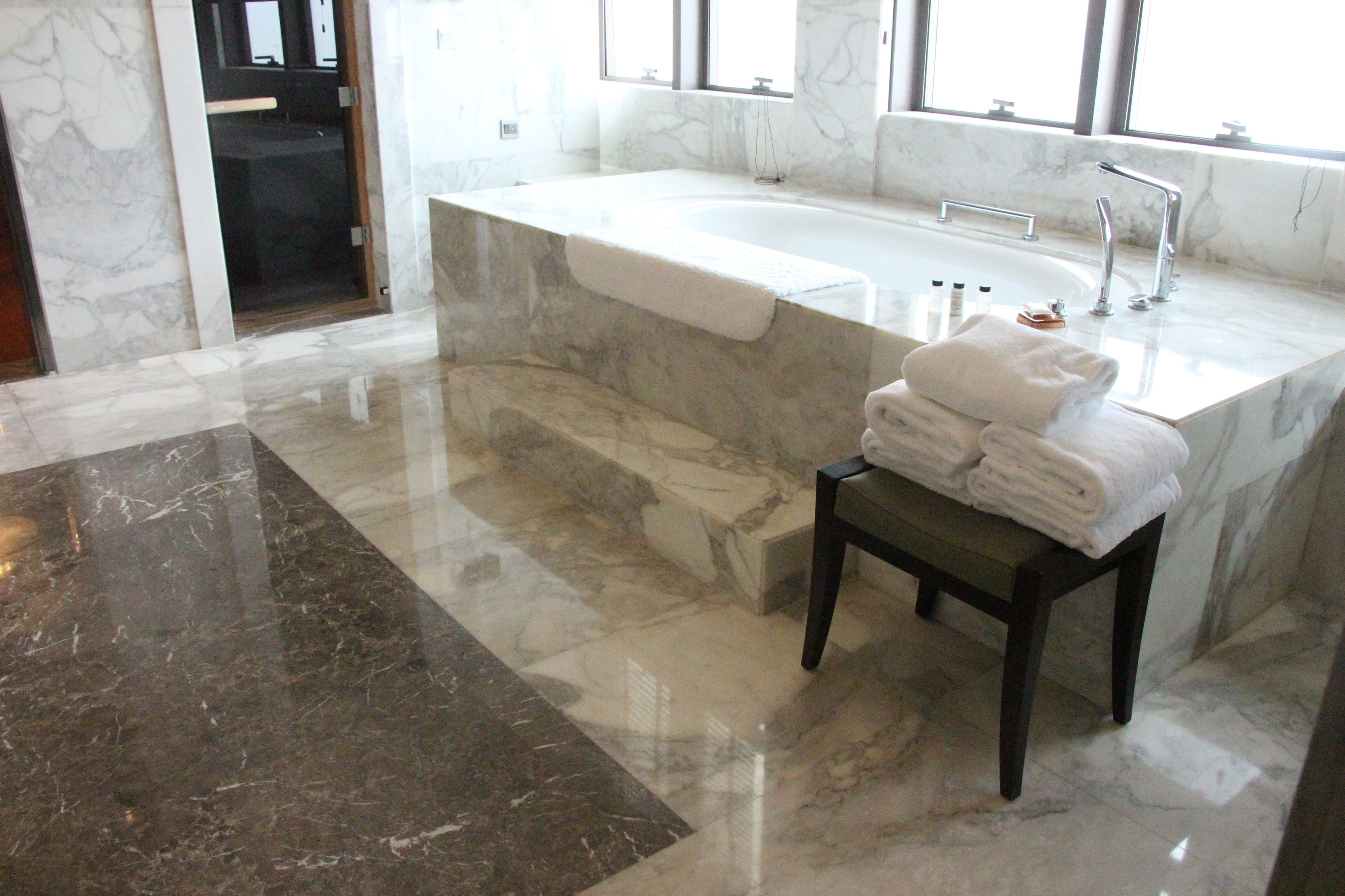 Ein modernes Badezimmer mit einem мраморной раковиной, einer großzügigen Badewanne und einem dunklen Holzschemel mit Handtüchern.