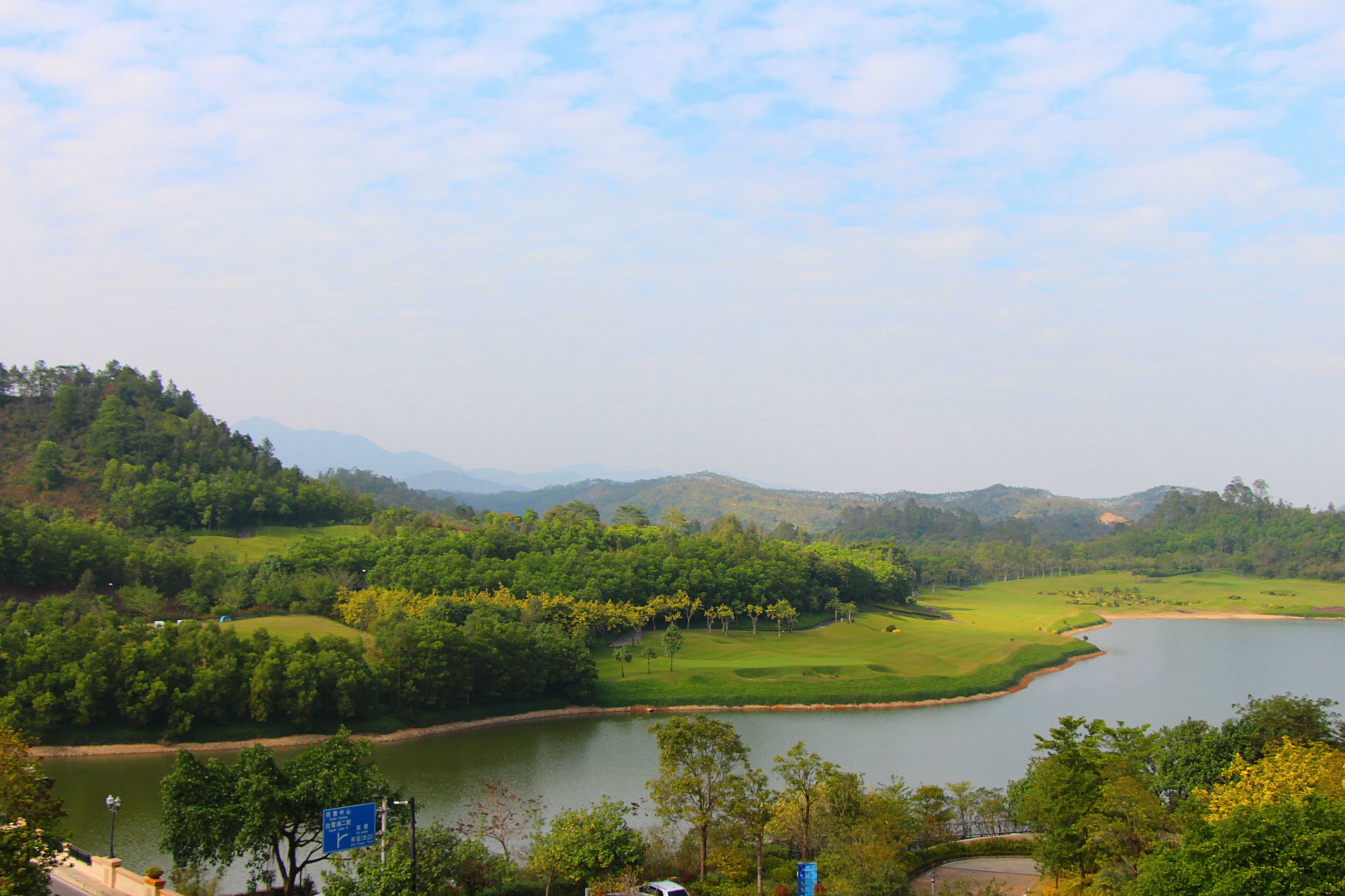 A golf course with a lake, surrounded by hills and trees.
