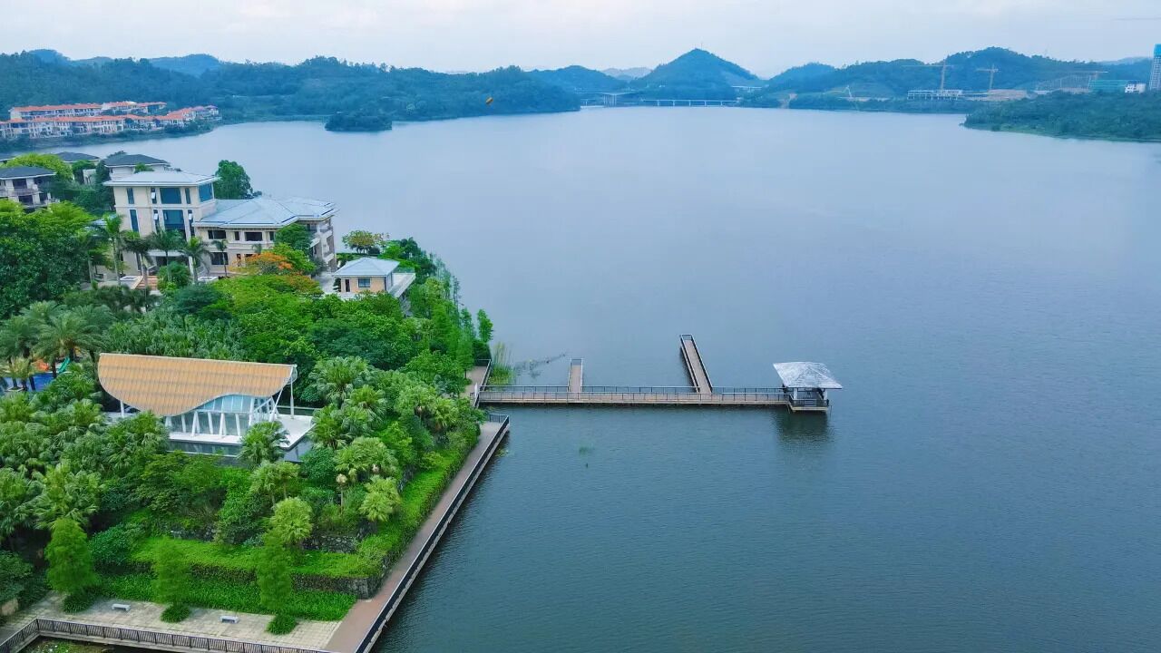 A lakeside property with a dock extending into the water, surrounded by lush greenery and modern buildings.