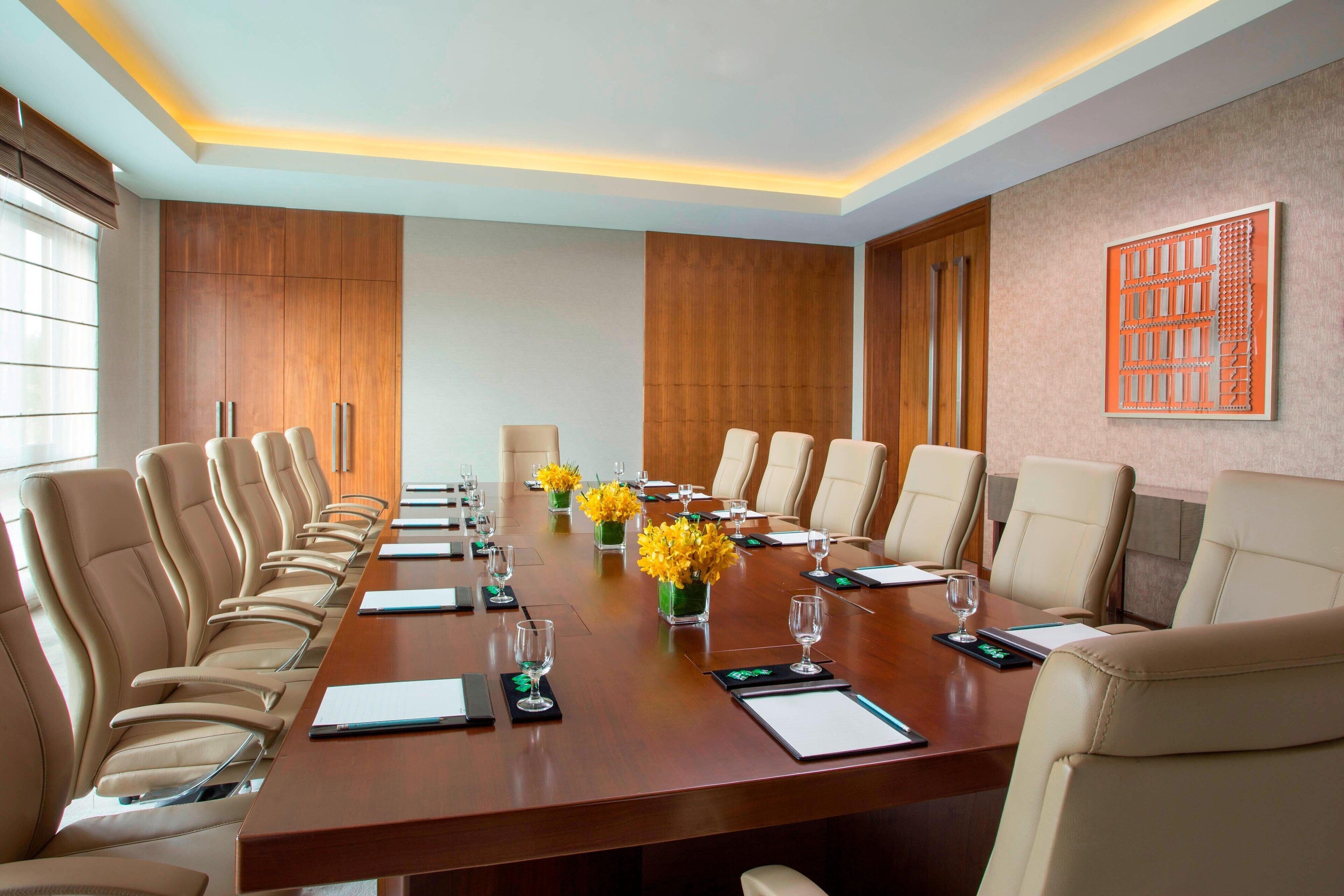 Uma sala de conferências com uma mesa comprida, várias cadeiras e arranjos florais.