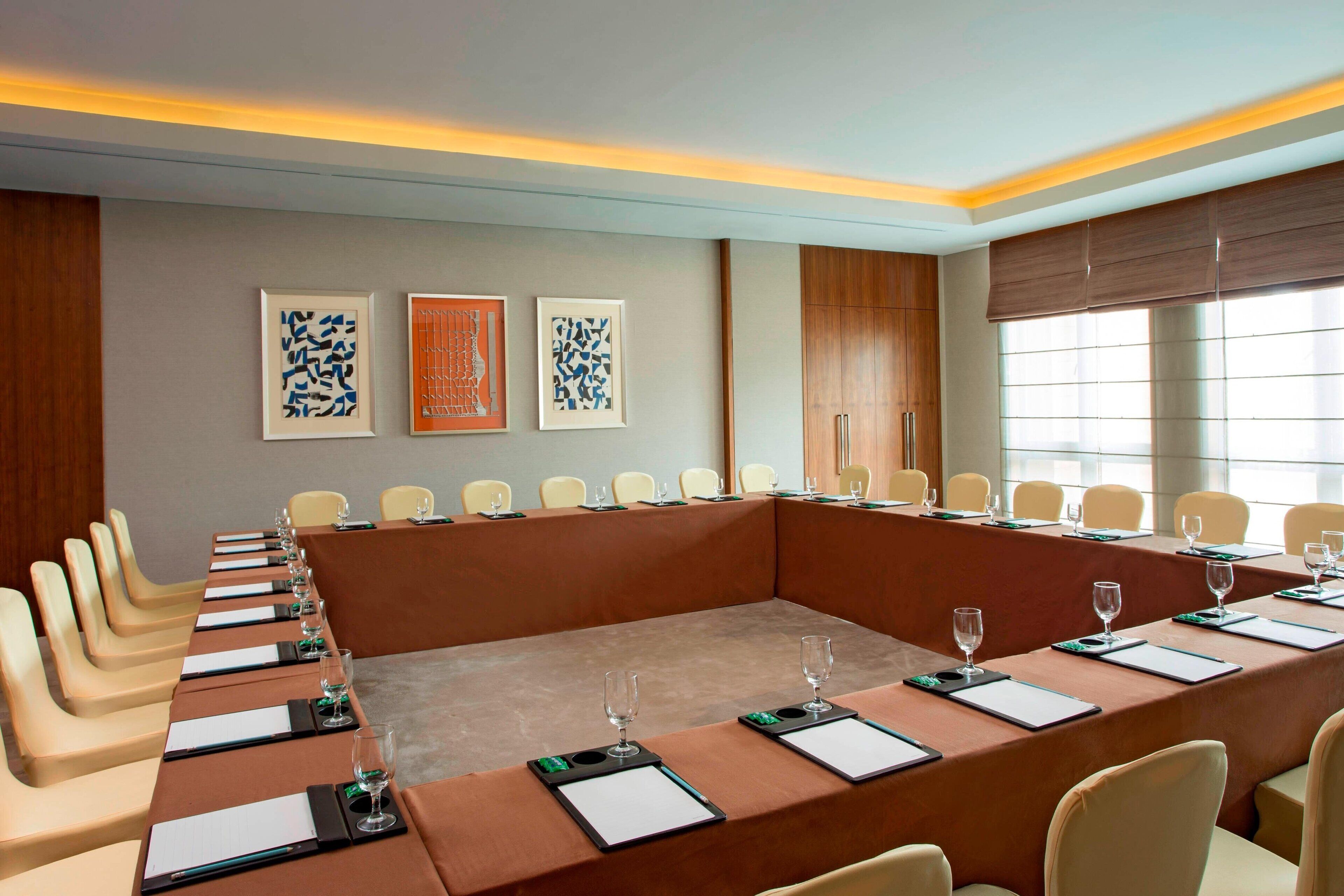 A conference room with a long table, chairs, and framed artwork on the wall.