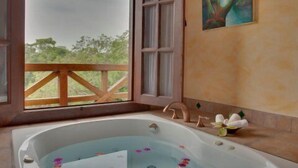 Eine große Badewanne mit Wasser und Blütenblättern, eine Holzterrasse im Freien und ein Gemälde an der Wand.