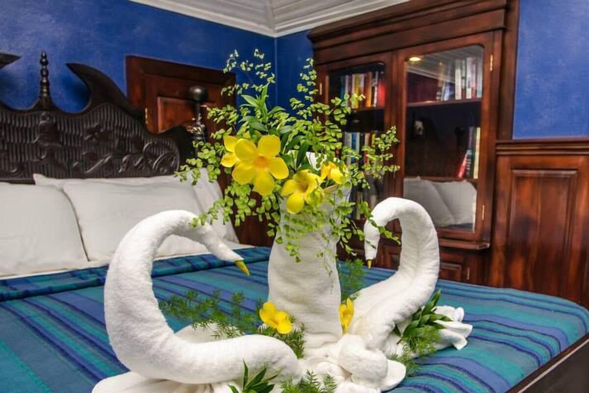 Una cama con una colcha azul y verde a rayas, un florero blanco con flores amarillas y una escultura decorativa de un cisne.