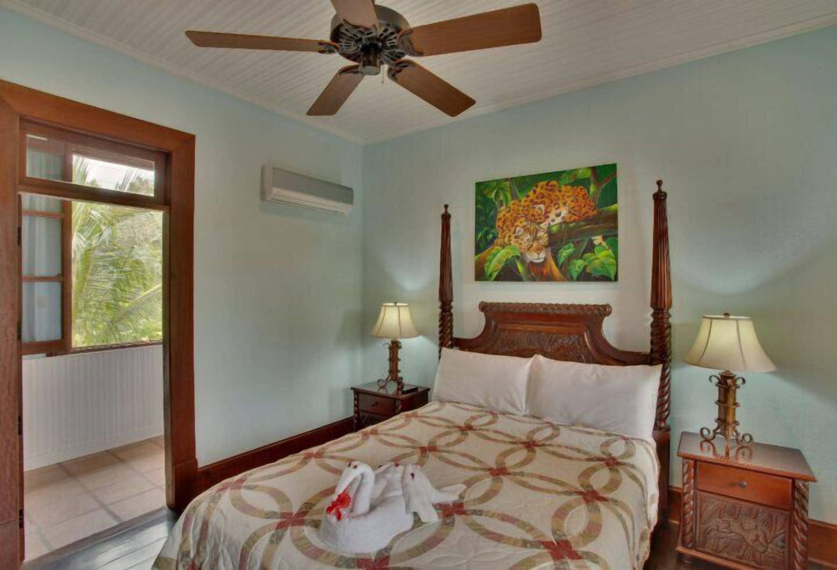 A bedroom with a four-poster bed, a ceiling fan, a painting of a leopard, and two bedside lamps.