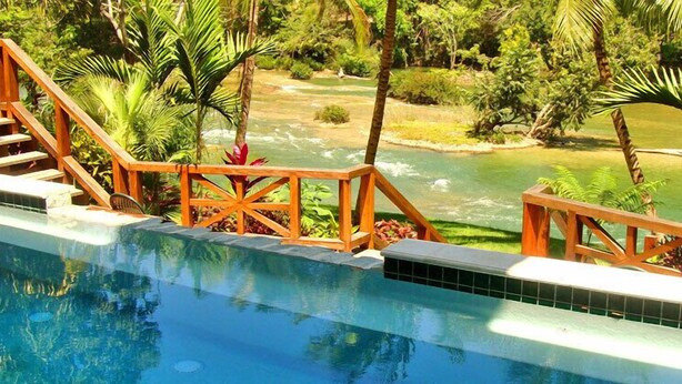 Ein Pool mit Holzgeländern und Blick auf einen Fluss und viel Grün.