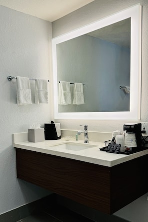 Enjoy a clean and minimalist bathroom with a large mirror, sink, and dark wood vanity.
