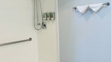 Zona de ducha con cabezal de ducha de mano, barras de apoyo y un perchero para toallas.