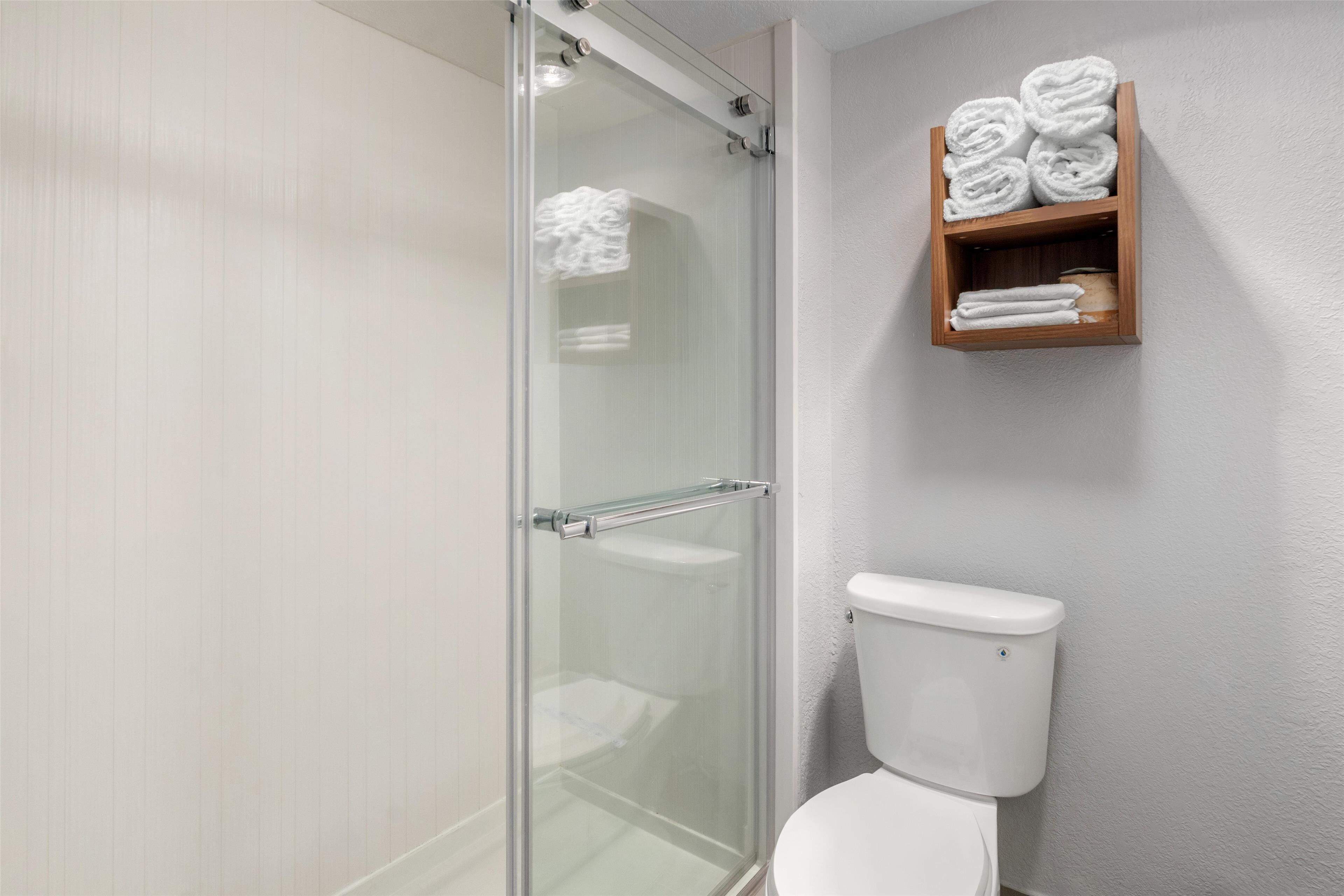 A bathroom with a glass shower enclosure, a white toilet, and a wooden towel rack with towels.