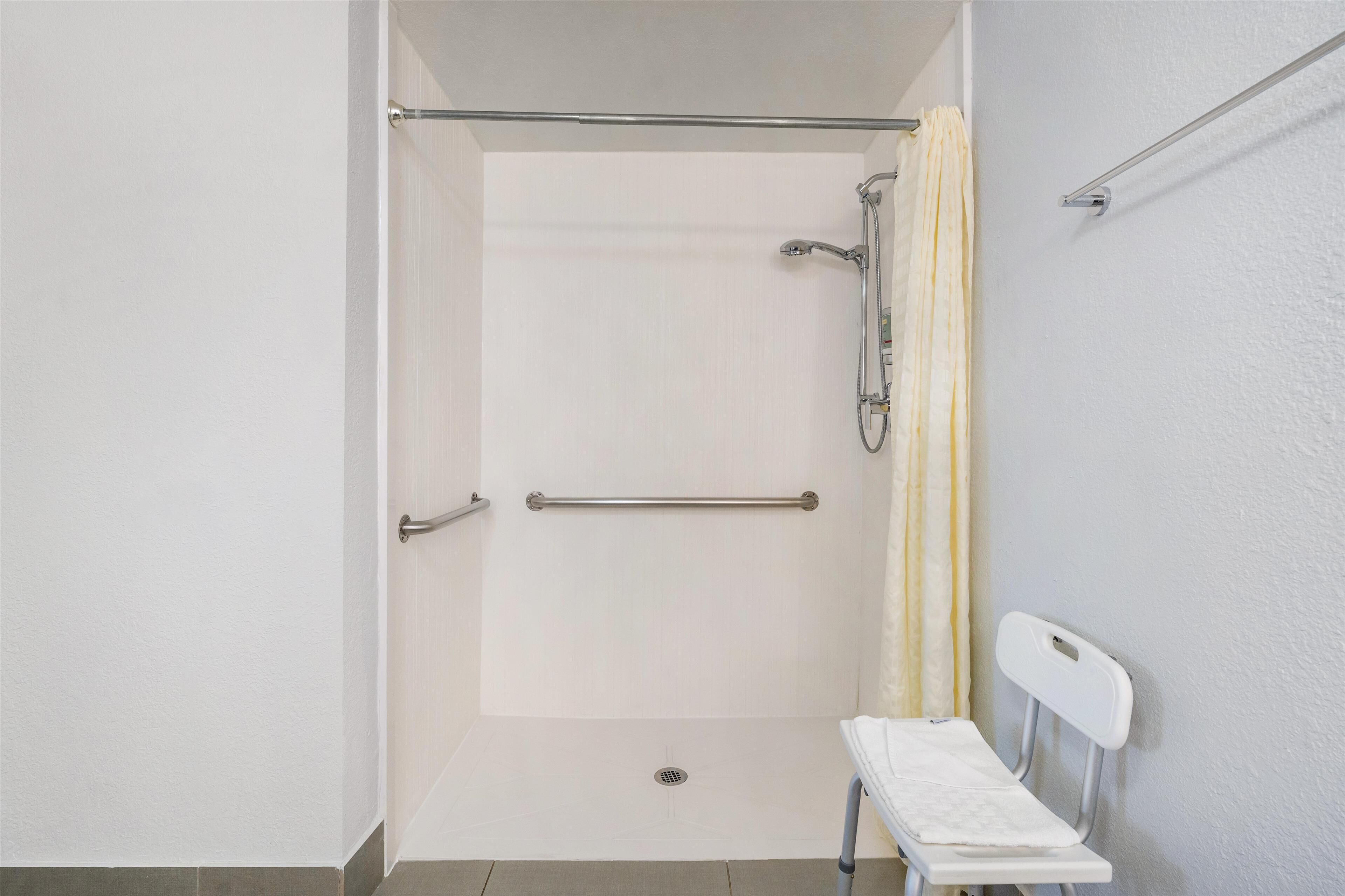 A shower area with a white tiled wall, a grab bar, a showerhead, and a towel rack.