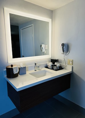Bathroom features a large mirror, sink, and dark vanity with a hairdryer and phone charger mounted on the wall.