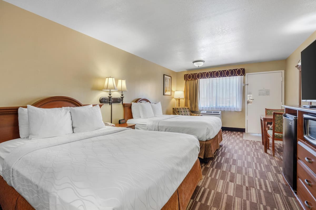 A hotel room with two beds, a desk, a refrigerator, and a window with curtains.