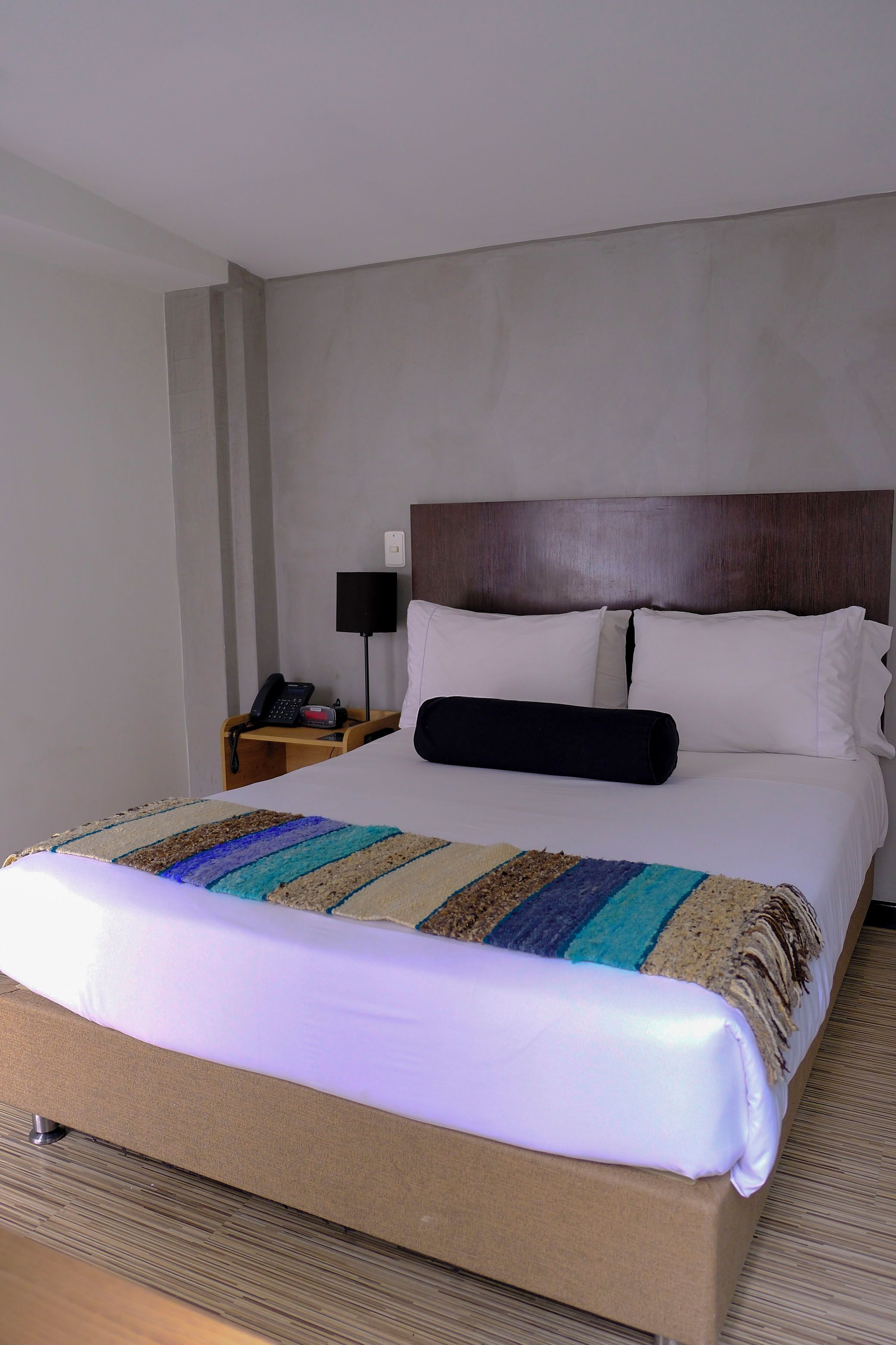A hotel room with a large bed, a wooden headboard, a bedside table with a lamp, and a phone.