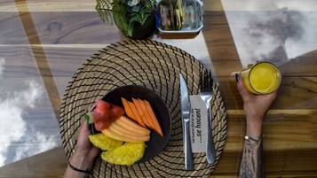 A table with a woven placemat, a plate of fruit, a knife and fork, a glass of juice, and a small plant.
