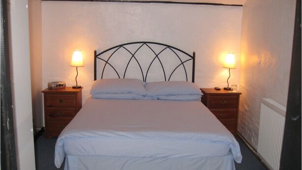 A single bed with a metal headboard, two bedside tables with lamps, and a radiator on the wall. - The Woodlands (Ely)