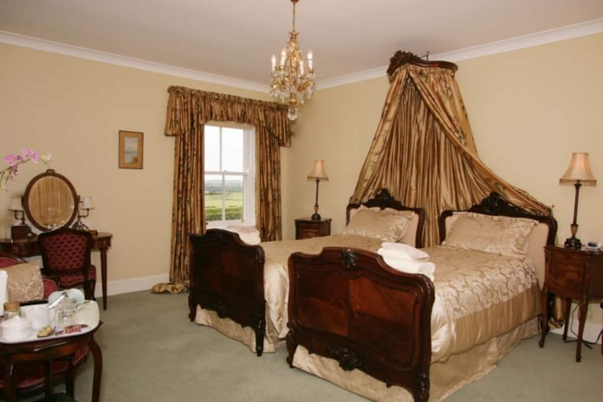 Een slaapkamer met een hemelbed, een kroonluchter en uitzicht op de omgeving.