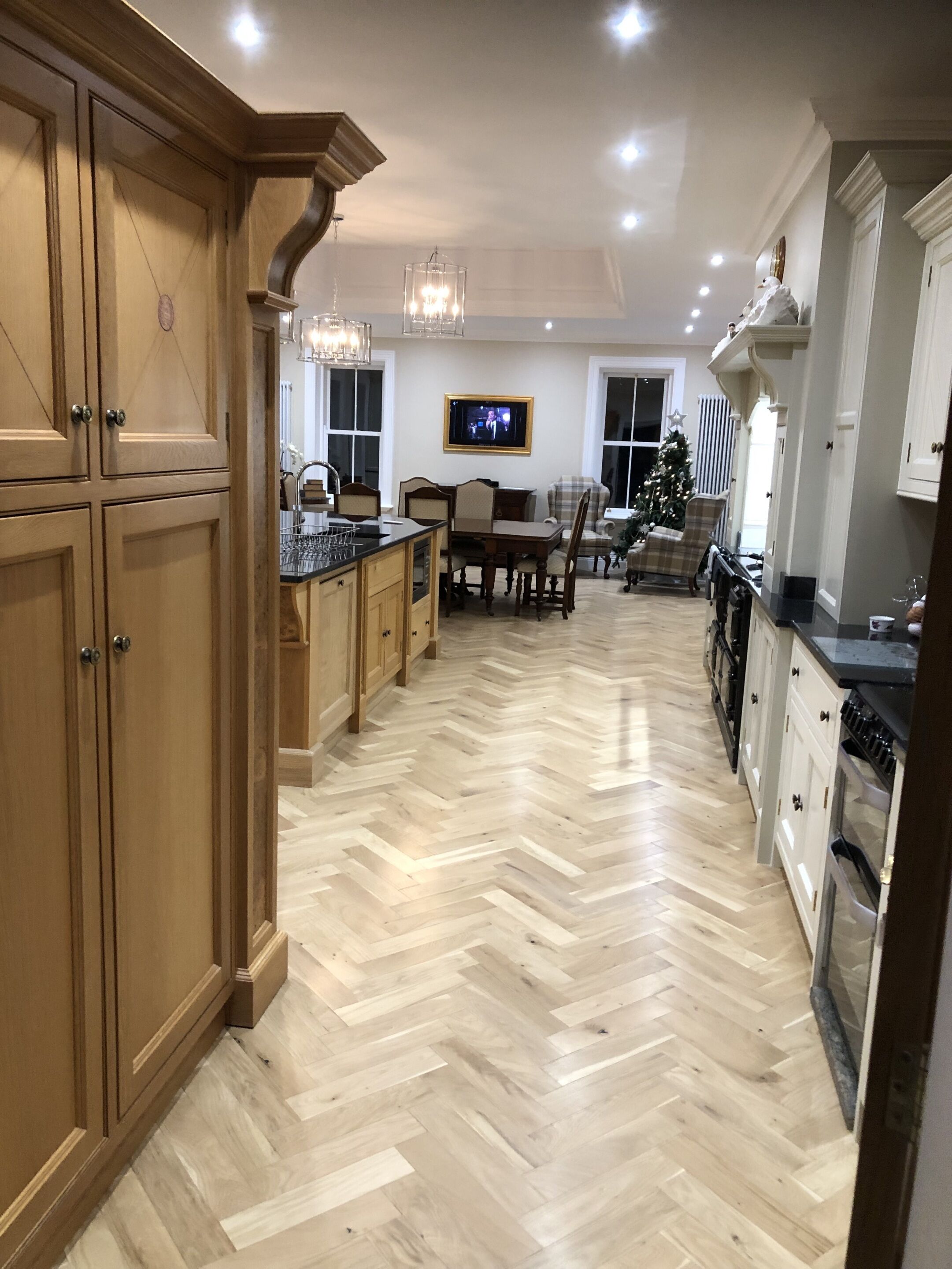 A spacious kitchen with wooden cabinetry, a herringbone floor pattern, and a dining area with a Christmas tree.