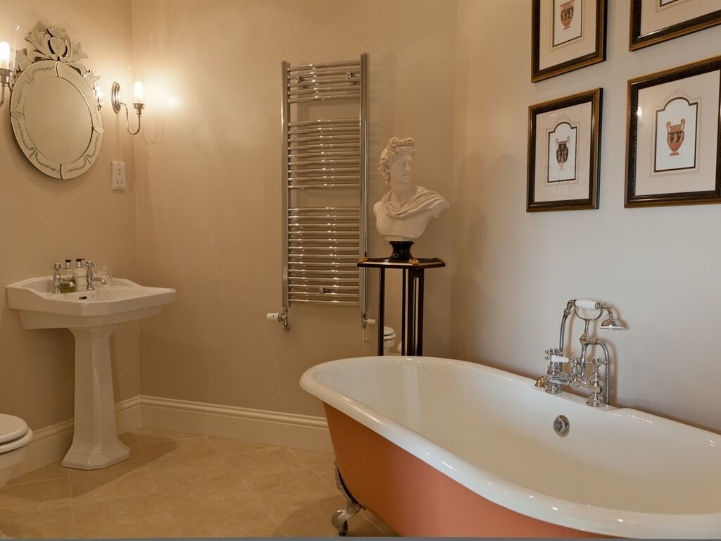 A bathroom with a pedestal sink, a freestanding bathtub, a towel rack, a mirror, and framed artwork on the wall.