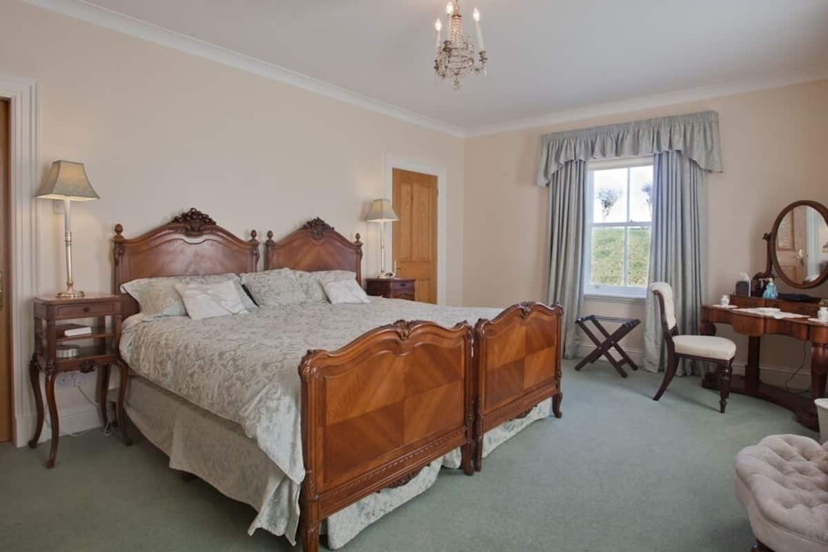 Een klassieke slaapkamer met een groot houten bed, twee nachtkastjes, een bureau, een stoel en een kroonluchter.