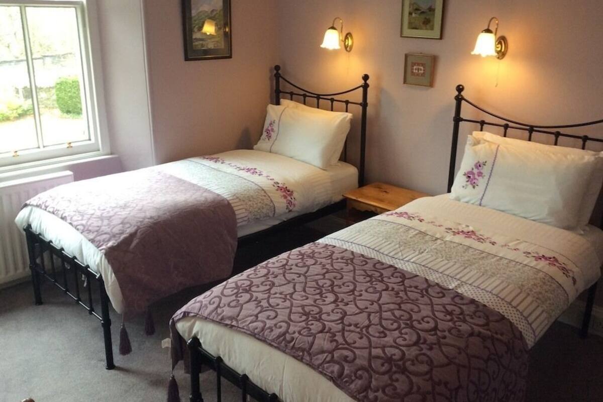 Two twin beds with headboards, a window, and wall-mounted light fixtures.