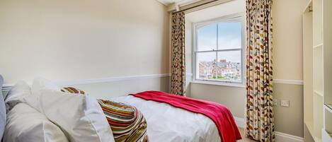 A bedroom with a bed, a window with curtains, and a view of buildings outside.
