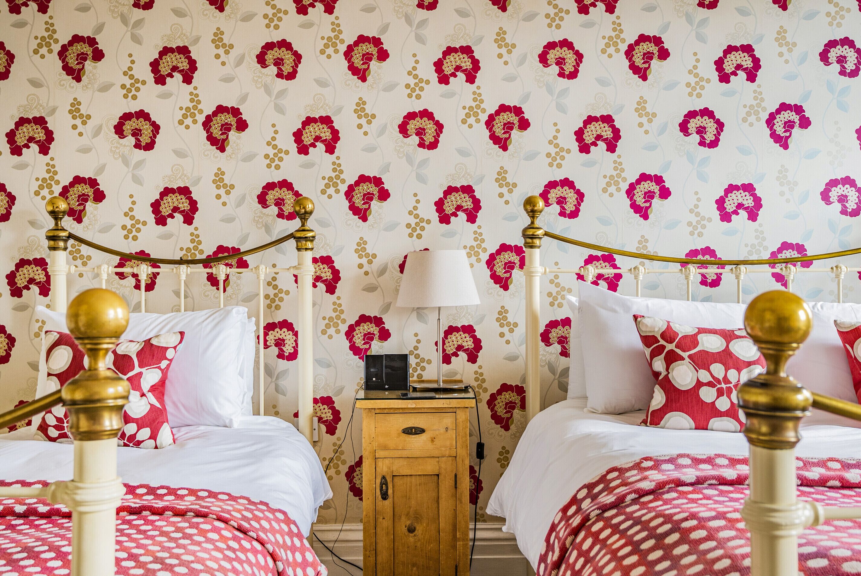A bedroom with two beds, a wooden nightstand, and a wall with floral wallpaper.