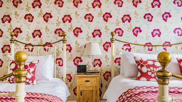 A bedroom with two beds, a wooden nightstand, and a wall with floral wallpaper.